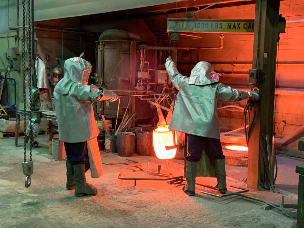 Two metal workers prepare to pour molten metal.