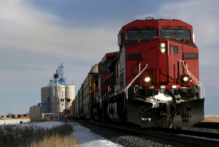 A freight train stopped near a farm grain elevator.