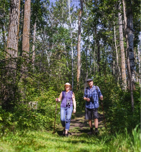 Two birdwatchers walk through a wooded greenspace.